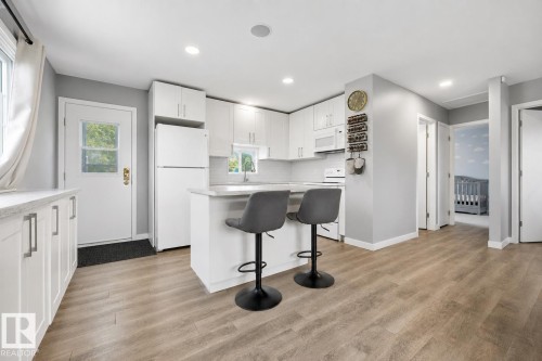 Modern kitchen featuring white cabinetry, light-toned countertops, and wood-finish flooring - 4810 55 Avenue, Beaumont, AB - Indoor Photo Showing Kitchen