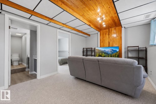 Carpeted living space featuring a wood-panel accent wall and ceiling with recessed lighting - 4810 55 Avenue, Beaumont, AB - Indoor