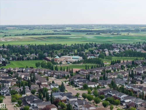 Expansive aerial perspective showcasing a residential neighborhood with numerous detached homes, mature trees, green spaces, and a large recreational field - 4810 55 Avenue, Beaumont, AB - Outdoor With View
