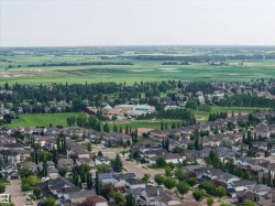 Expansive aerial perspective showcasing a residential neighborhood with numerous detached homes, mature trees, green spaces, and a large recreational field - 