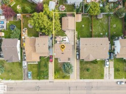 Aerial perspective highlighting a residential property with a paved driveway, front lawn, and established trees - 