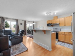 Open-concept living space featuring wood-finish flooring, a kitchen with light wood cabinetry and stainless steel appliances, a breakfast bar, and sliding glass doors to the exterior - 