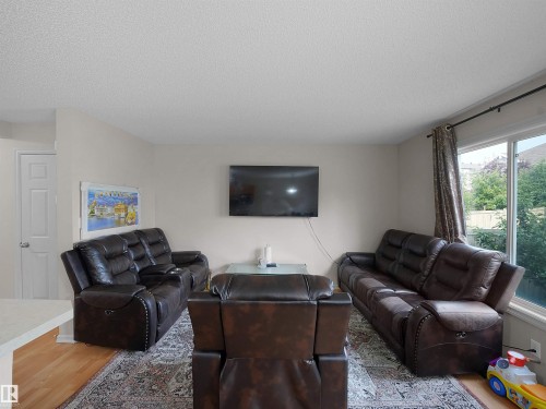 Living area featuring wood-finish flooring, a wall-mounted television, and a large window with exterior landscaping - 8111 7 Avenue Sw, Edmonton, AB - Indoor Photo Showing Living Room