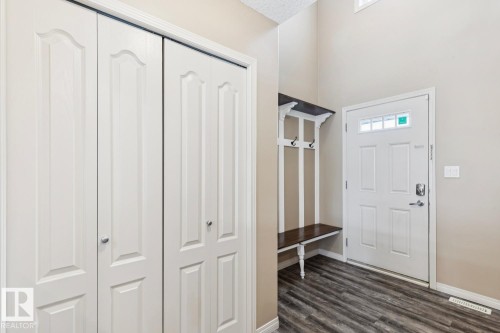 Entryway with wood-finish flooring, a built-in bench with hooks, a white panel door with transom windows, and white bifold closet doors - 16765 119 Street Nw, Edmonton, AB - Indoor Photo Showing Other Room