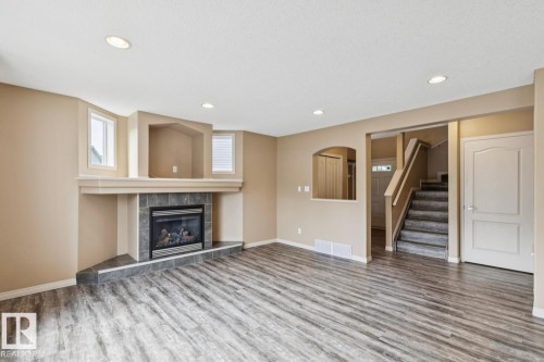 Spacious living area featuring wood-finish flooring, a tiled fireplace with mantel, recessed lighting, and ample natural light from multiple windows - 16765 119 Street Nw, Edmonton, AB - Indoor Photo Showing Living Room With Fireplace