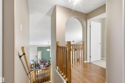 Upper-level hallway featuring wood-finish flooring, a wood balustrade, an arched doorway, and light neutral wall paint - 