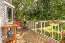 Wood-finish deck with white railing, featuring a large bay window and lush surrounding greenery - 