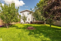 Expansive backyard featuring a green lawn, mature trees, and a fire pit - 