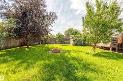 Expansive rear yard featuring a large lawn, mature trees, and a brick fire pit - 
