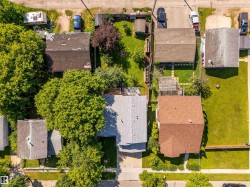 Property featuring a light gray shingle roof, mature trees providing canopy, and a green lawn area - 