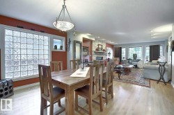 Spacious open-concept living area featuring light wood flooring, a dining area with a wood table and chairs, and a living room with a large area rug and a stone fireplace - 