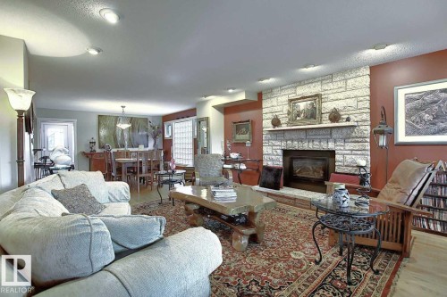 The living space features a stone-clad fireplace and a patterned area rug over hardwood flooring - 11126 52 Street Nw, Edmonton, AB - Indoor Photo Showing Living Room With Fireplace