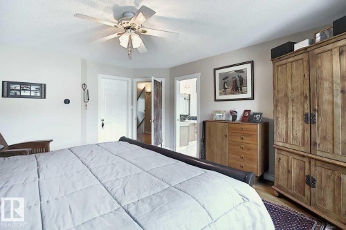 This bedroom features a ceiling fan, hardwood flooring, and a wardrobe with a natural wood finish - 11126 52 Street Nw, Edmonton, AB - Indoor Photo Showing Bedroom