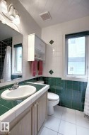Bathroom with white floor tiles, a window, and a vanity featuring a white sink and wood-toned cabinetry - 