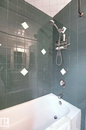 Bathroom featuring a bathtub and shower combination with green tiled walls and decorative white diamond accents - 11126 52 Street Nw, Edmonton, AB - Indoor Photo Showing Bathroom