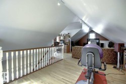 This expansive third floor space features light hardwood flooring, a white railing, and track lighting - 