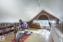 Versatile loft space featuring hardwood floors, track lighting, and a large arched window with patterned blinds - 