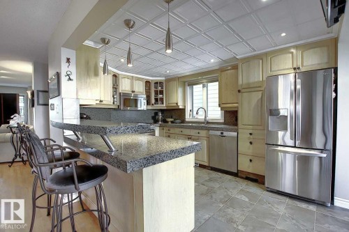 The kitchen features light wood cabinetry, a granite breakfast bar, stainless steel appliances, and a tiled ceiling with pendant lighting - 11126 52 Street Nw, Edmonton, AB - Indoor Photo Showing Kitchen With Upgraded Kitchen