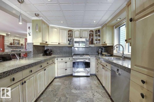 The kitchen features light-toned cabinetry, granite countertops, and stainless steel appliances, including a range and dishwasher - 11126 52 Street Nw, Edmonton, AB - Indoor Photo Showing Kitchen With Double Sink