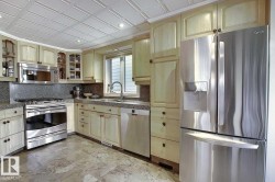 This kitchen features light wood cabinetry, stone countertops, and stainless steel appliances including a refrigerator, dishwasher, and stove with an overhead microwave - 