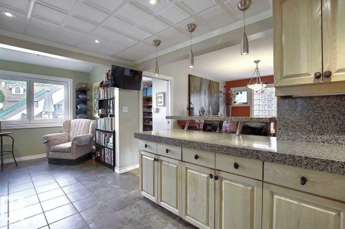 The property offers a kitchen with granite countertops, light-colored cabinetry, and pendant lighting, featuring a view into an adjacent area with a large window - 11126 52 Street Nw, Edmonton, AB - Indoor