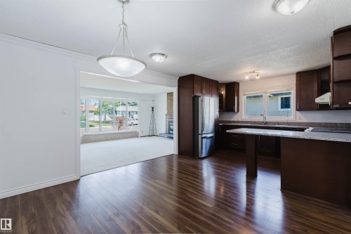Open concept interior featuring wood-finish flooring, a kitchen with dark cabinetry and light countertops, stainless steel appliances, and a living area with a large picture window - 11115 39A Avenue Nw, Edmonton, AB - Indoor Photo Showing Kitchen With Double Sink