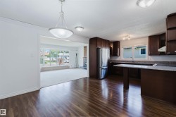 Open concept interior featuring wood-finish flooring, a kitchen with dark cabinetry and light countertops, stainless steel appliances, and a living area with a large picture window - 