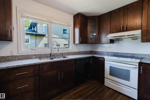 Kitchen featuring dark wood-finish cabinetry, granite-style countertops, stainless steel double-basin sink, white electric range with overhead ventilation, and wood-finish flooring - 11115 39A Avenue Nw, Edmonton, AB - Indoor Photo Showing Kitchen With Double Sink