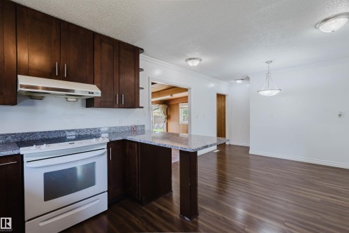 Kitchen with dark wood cabinetry, light granite countertops, white oven with range hood, and wood-finish flooring extending into the open concept space - 11115 39A Avenue Nw, Edmonton, AB - Indoor Photo Showing Kitchen