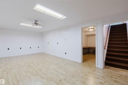 Spacious room featuring light wood-finish flooring, white walls, and a ceiling fan with integrated lighting - 