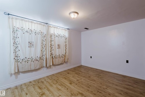 Spacious interior featuring wood-finish flooring, white baseboards, and bright white walls - 11115 39A Avenue Nw, Edmonton, AB - Indoor Photo Showing Other Room