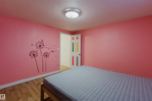 Room featuring wood-finish flooring, a flush-mount ceiling light fixture, and a white interior door with decorative color panels - 11115 39A Avenue Nw, Edmonton, AB - Indoor Photo Showing Bedroom