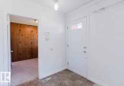Entryway featuring a white door with upper window panes, textured tile flooring, and crisp white walls - 