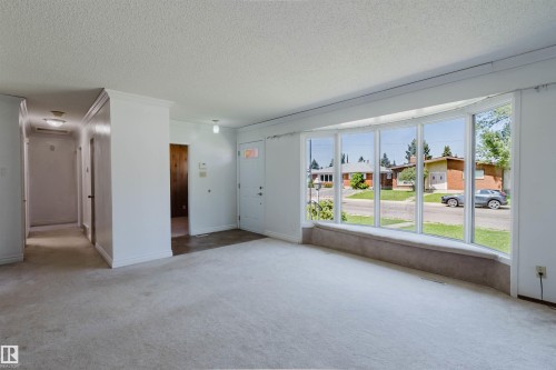 Living space featuring a prominent bay window with street scenery, light-toned carpeting, white walls, and a hallway entry - 11115 39A Avenue Nw, Edmonton, AB - Indoor Photo Showing Other Room