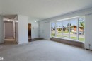 Living space featuring a prominent bay window with street scenery, light-toned carpeting, white walls, and a hallway entry - 11115 39A Avenue Nw, Edmonton, AB  - Indoor Photo Showing Other Room 