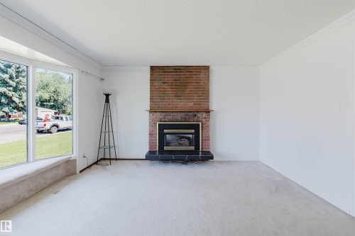 Living area with bay window, brick fireplace with mantel, black hearth, and light-toned carpeting - 11115 39A Avenue Nw, Edmonton, AB - Indoor Photo Showing Living Room With Fireplace