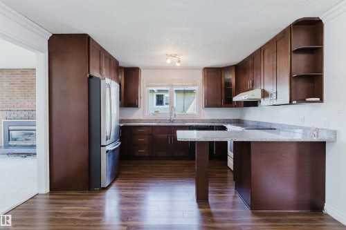 Kitchen featuring dark wood cabinetry, stainless steel appliances, light granite countertops, and wood-finish flooring - 11115 39A Avenue Nw, Edmonton, AB - Indoor Photo Showing Kitchen