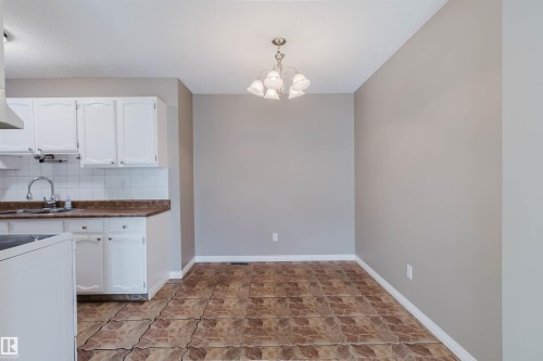 Kitchen and dining area featuring white cabinetry, a stainless steel sink with a high-arc faucet, and a tiled backsplash - 134 Callingwood Place Nw, Edmonton, AB - Indoor Photo Showing Kitchen With Double Sink