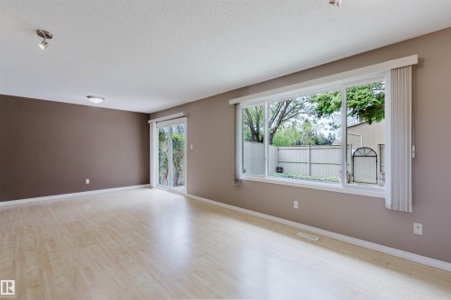 Spacious room featuring light wood-finish flooring, a large picture window, and a sliding glass door - 134 Callingwood Place Nw, Edmonton, AB - Indoor Photo Showing Other Room
