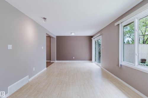 Spacious room featuring wood-finish flooring, light grey and accent brown walls, a sliding glass door, and large windows - 134 Callingwood Place Nw, Edmonton, AB - Indoor Photo Showing Other Room
