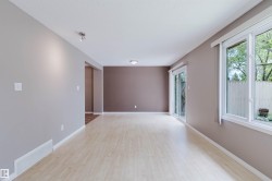 Spacious room featuring wood-finish flooring, light grey and accent brown walls, a sliding glass door, and large windows - 
