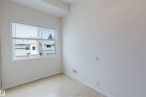 Bright room featuring a large window with horizontal blinds, light wood-finish flooring, and crisp white walls - 134 Callingwood Place Nw, Edmonton, AB - Indoor Photo Showing Other Room