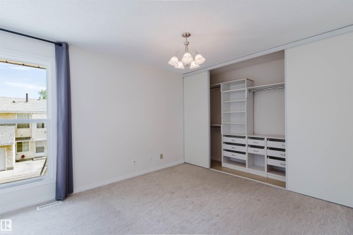 Carpeted room with a large window, a ceiling-mounted light fixture, and a built-in closet organization system featuring shelving, hanging rods, and drawers - 134 Callingwood Place Nw, Edmonton, AB - Indoor Photo Showing Other Room