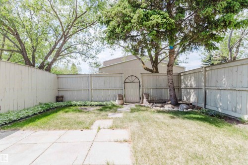 Fully fenced backyard featuring a mature tree, an arched garden gate, a concrete patio, and garden beds with established groundcover - 134 Callingwood Place Nw, Edmonton, AB - Outdoor