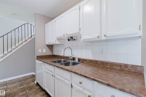 Kitchen area featuring white cabinetry, a double basin stainless steel sink with a high-arc faucet, and a white tile backsplash - 134 Callingwood Place Nw, Edmonton, AB - Indoor Photo Showing Kitchen With Double Sink