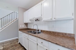Kitchen area featuring white cabinetry, a double basin stainless steel sink with a high-arc faucet, and a white tile backsplash - 