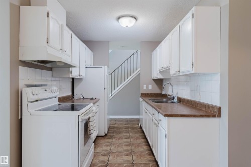 Galley kitchen featuring white cabinetry, laminate countertops, white tile backsplash, and ceramic tile flooring - 134 Callingwood Place Nw, Edmonton, AB - Indoor