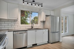 Kitchen featuring white shaker-style cabinetry with chrome hardware, subway tile backsplash, and dark countertops - 