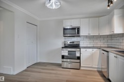 Kitchen featuring stainless steel appliances, white cabinetry, subway tile backsplash, and wood-finish flooring - 