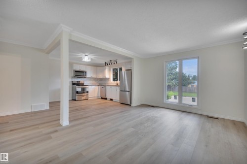 Open-concept living area with wood-finish flooring, crown molding, and a kitchen featuring stainless steel appliances, white cabinetry, and a subway tile backsplash - 3607 53 Street, Wetaskiwin, AB - Indoor